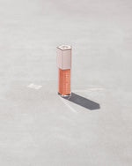 A closed tube of Gloss Bomb Universal Lip Luminizer in the shade Champ Stamp Fantasy on a grey background.