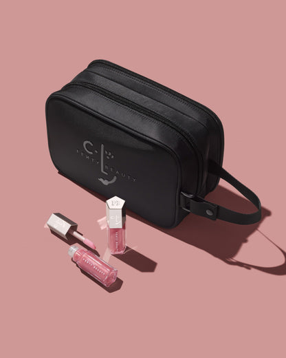 CLF makeup bag and two tubes of Gloss Bomb Universal Lip Luminizer in shade Candy Soda on a pink background.