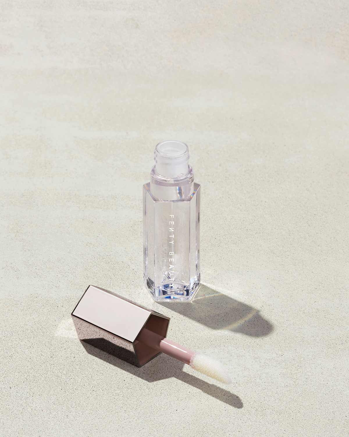 An open tube of Gloss Bomb Universal Lip Luminizer in the shade Glass Slipper on a grey background.