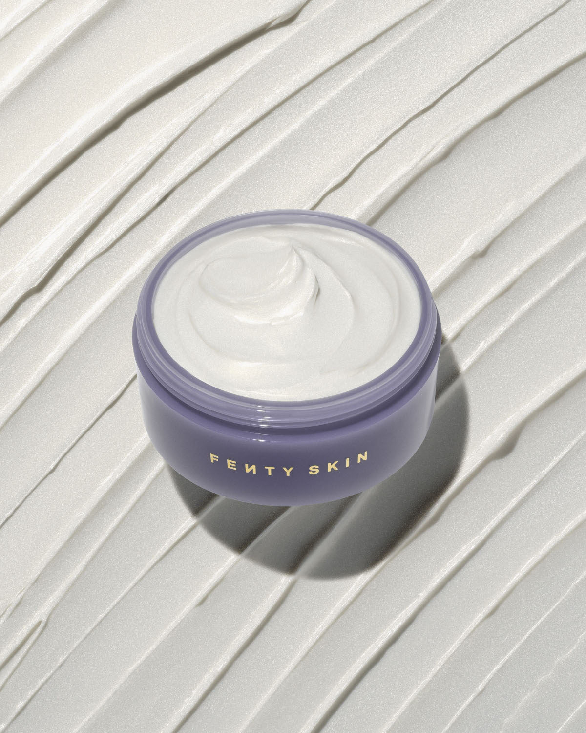 An open tub of Butta Drop Shimmering Whipped Oil Body Cream with Tropical Oils + Shea Butter on a textured smear background.
