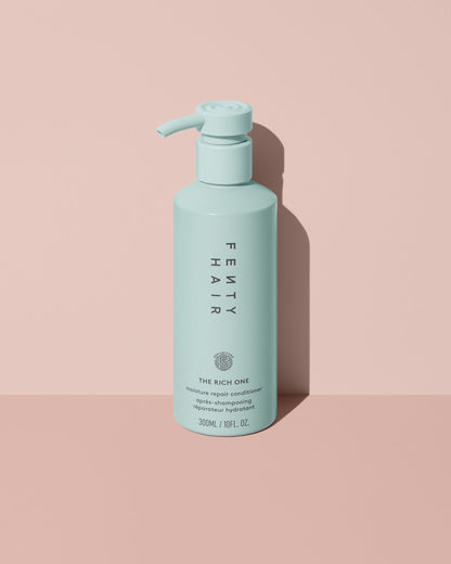 Fenty Hair The Rich One Moisture Repair Conditioner aluminum bottle with a pump on a pink background.